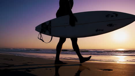 surfer carrying surfboard on beach at sunset