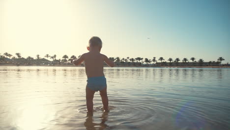 Active-boy-splashing-water-at-seaside.-Little-child-walking-at-summer-beach.