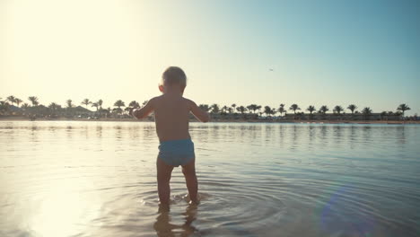 active boy splashing water at seaside. little child walking at summer beach.