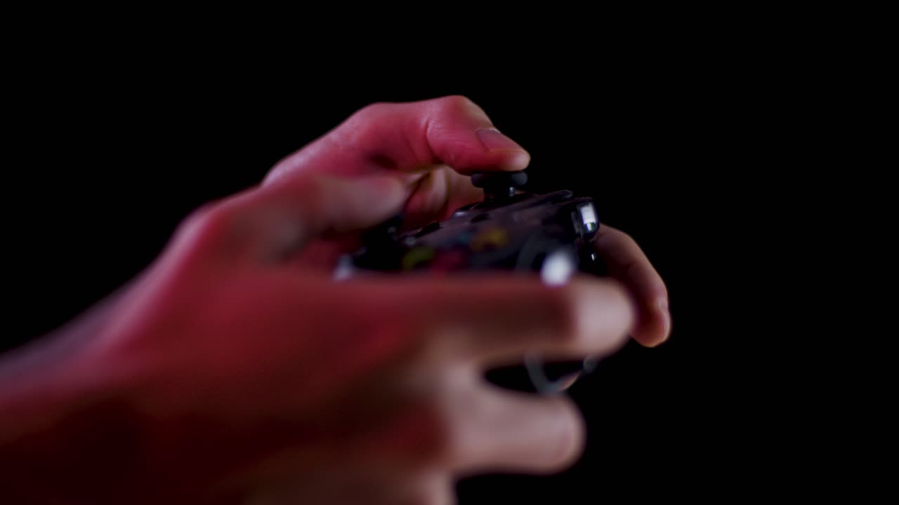 Playing video games in a darkened room with a black background close up on a controller joystick playing slowly