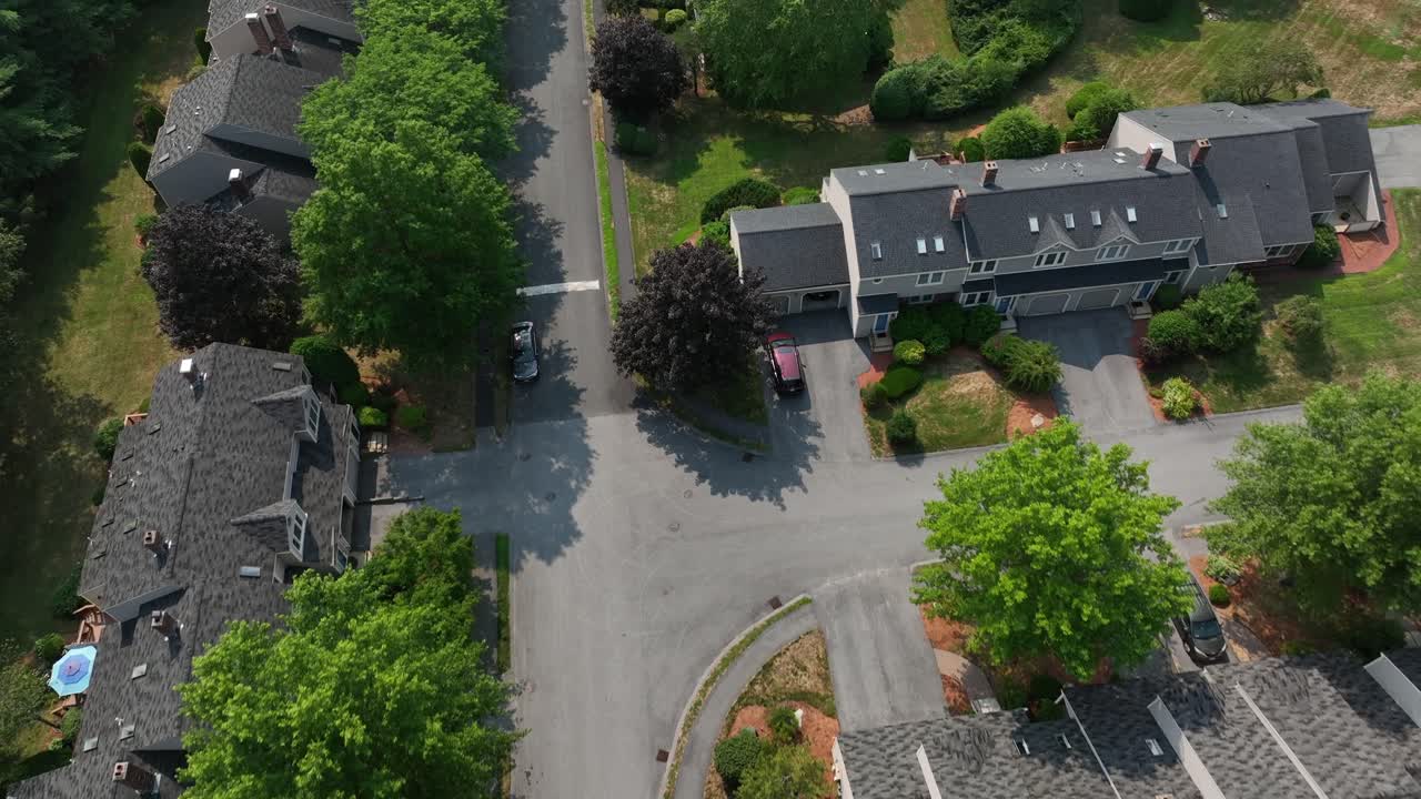 Aerial flyover modern grey townhouses with pitched roofs, tree-lined streets and shared walls in a quiet suburban neighborhood of Massachusetts. Swimming pool and tennis field for community