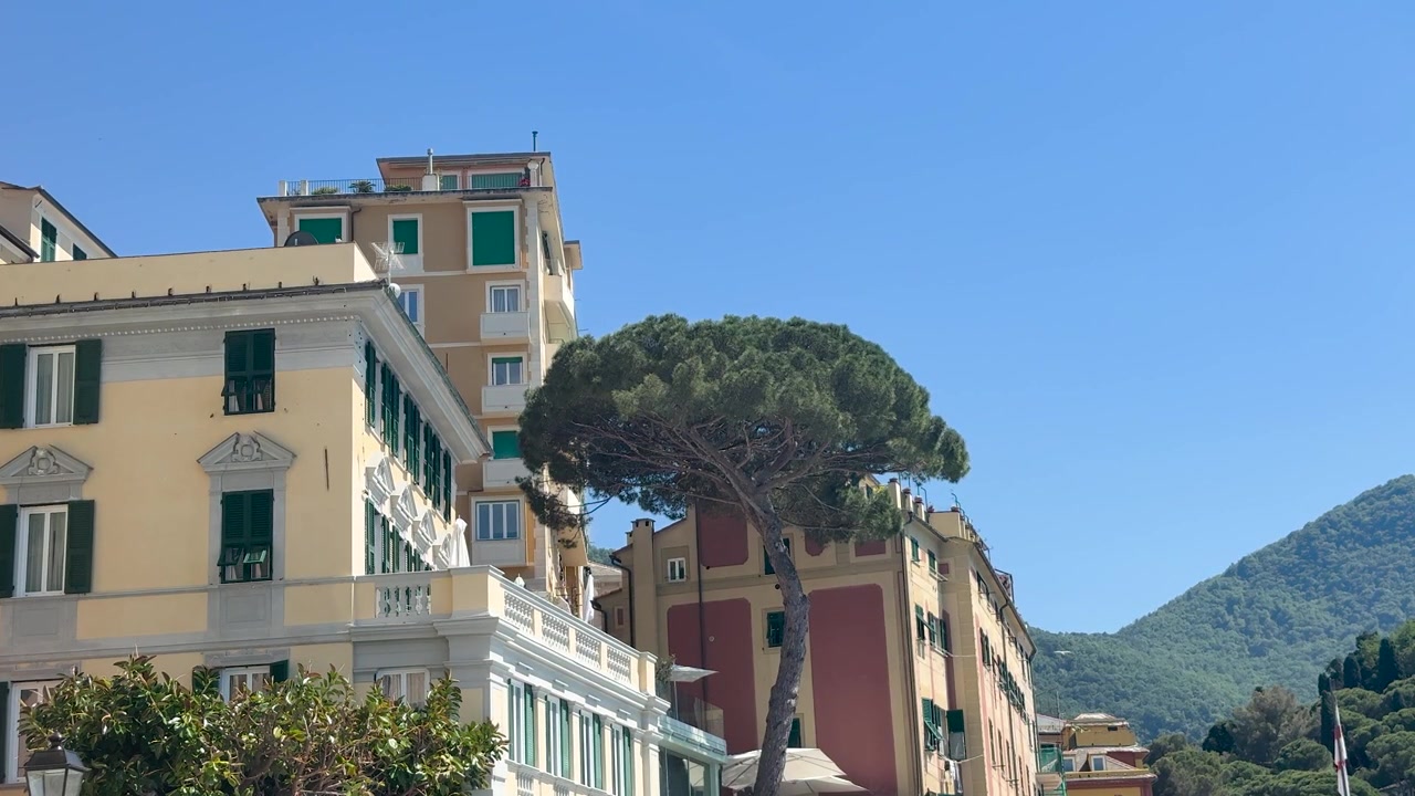 Inquadratura ampia statica di storici edifici residenziali della Riviera Italiana sotto un cielo azzurro limpido.