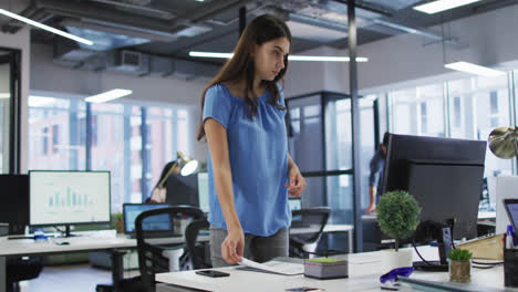 Portrait-of-caucasian-businesswoman-standing-next-to-desk-holding-document-and-smiling