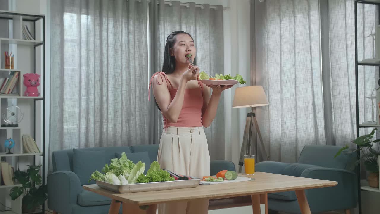 아시아 여성이 건강한 음식을 먹기 전에 미소 짓고 엄지손가락을 보여주고 집에서 카메라에 제스처를 합니다.