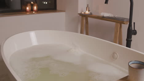 Weiße-Badewanne-Gefüllt-Mit-Wasser-Mit-Schaum-In-Einem-Mit-Kerzen-Dekorierten-Badezimmer