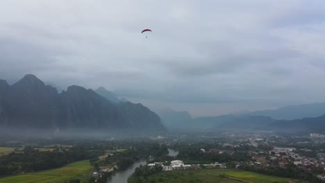 aerial view of paraglider soaring above vang vieng landscape in the evening above low level misty clouds layer
