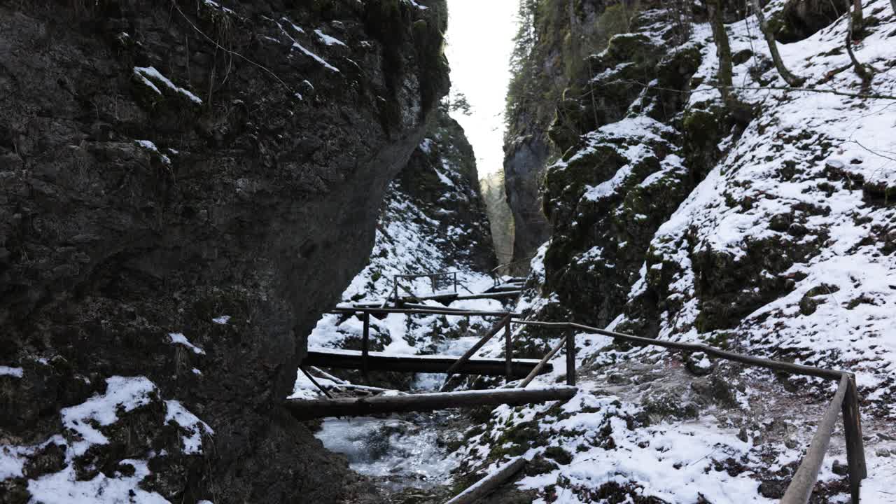 Holzbrücke zwischen schroffen, schneebedeckten Klippen im Winter