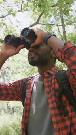 Vertical video of african american man using binoculars in park, slow motion