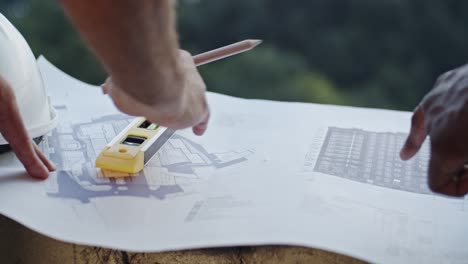 close up of the caucasian and african american male hands pointing something on the drafts and plans while men builders and architects working over the project.