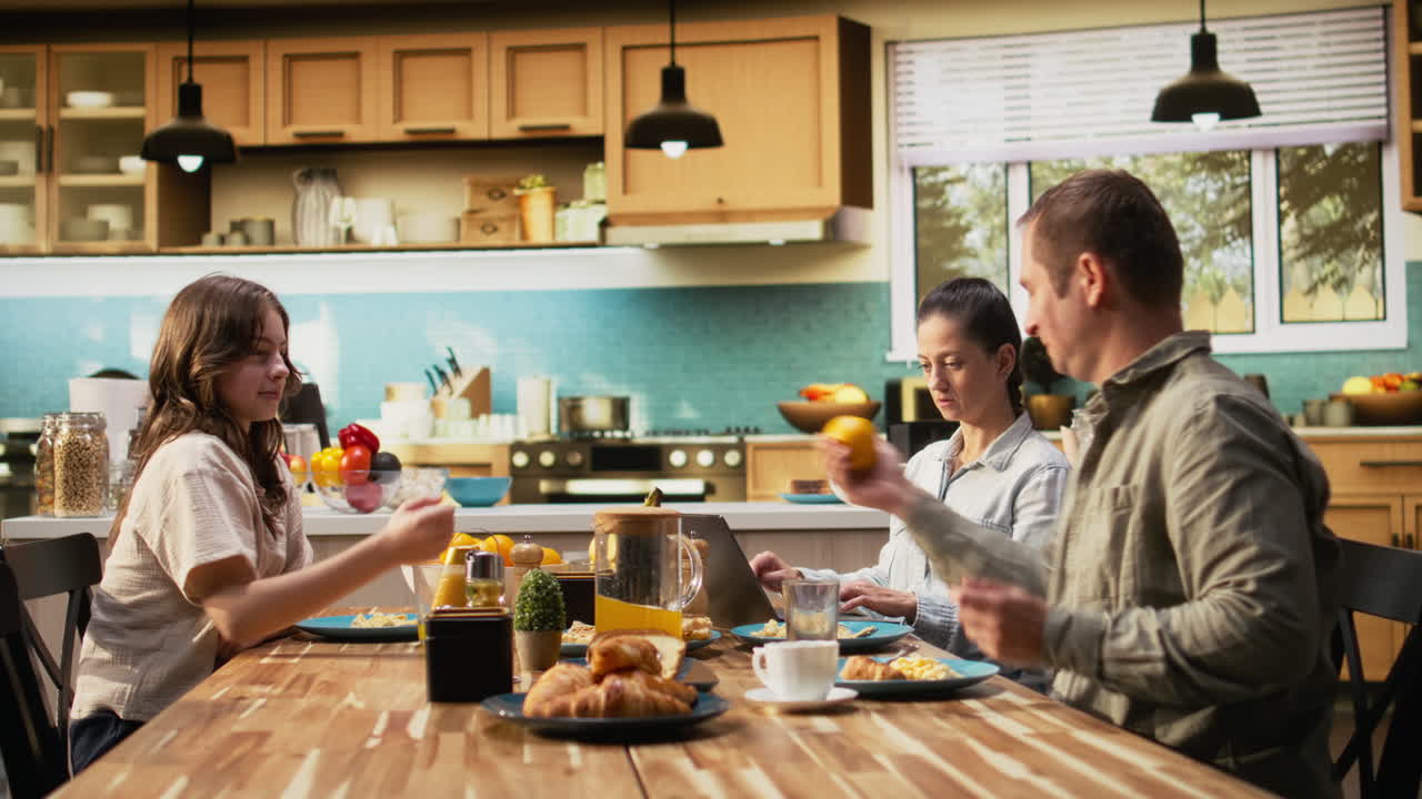 Mom doing remote work on laptop while pre-teen girl chats with his father