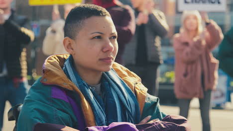 portrait of female protestor in wheelchair surrounded by marchers with placard on demonstration