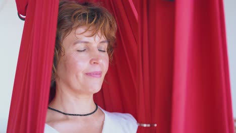 pretty woman sits with closed eyes in fly yoga hammock