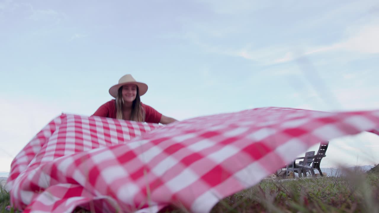 Kvinde arrangerer et picnictæppe på plænen.