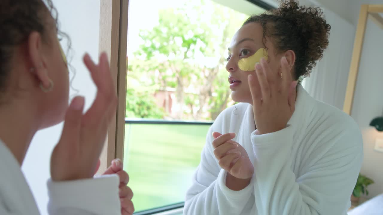 Donna afroamericana che tiene in mano patch dorati per il contorno occhi alla toeletta, applicandoli e levigandoli per la cura della pelle.