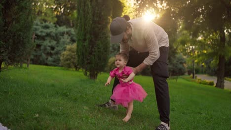 father helping daughter take her first steps in the park