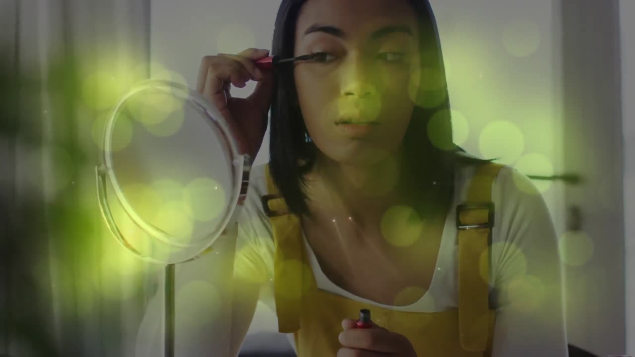 animación de manchas de luz sobre una mujer biracial aplicando rímel
