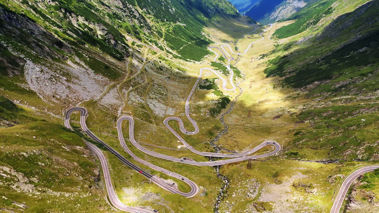 Cars run by the wavy highway on the mountains slopes. Drone footage over the picturesque road Transfagarash in Romania