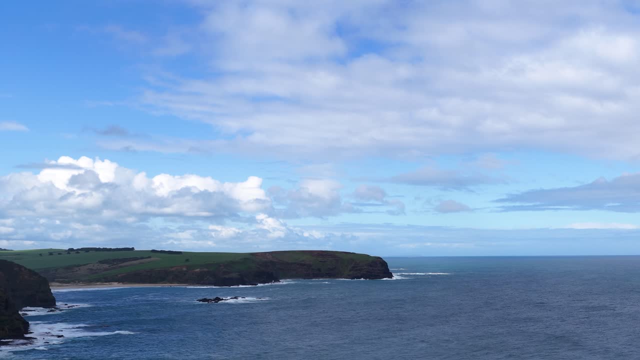 Camera pans across rugged coastal cliffs, blue ocean, and dramatic sky at Cape Schanck, Australia