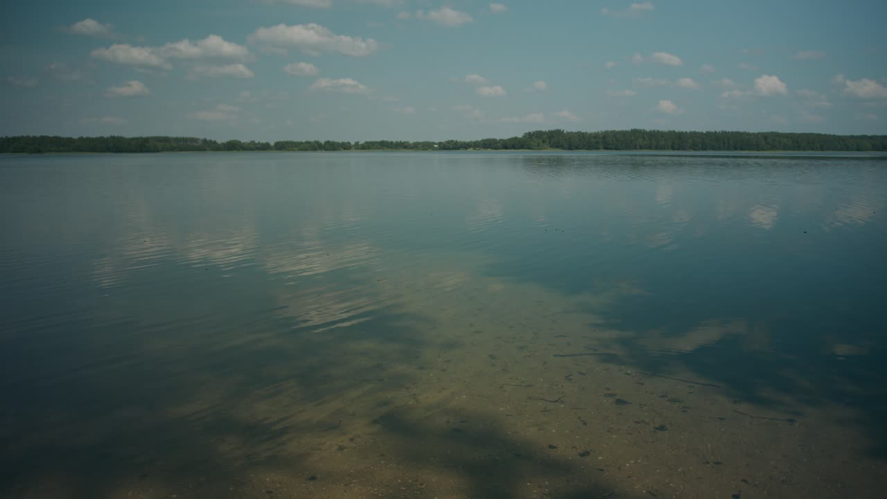 Las tranquilas aguas del lago reflejan un cielo escasamente nublado hasta la arboleda en el horizonte