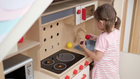 little girl playing in toy kitchen washing fruits in sink