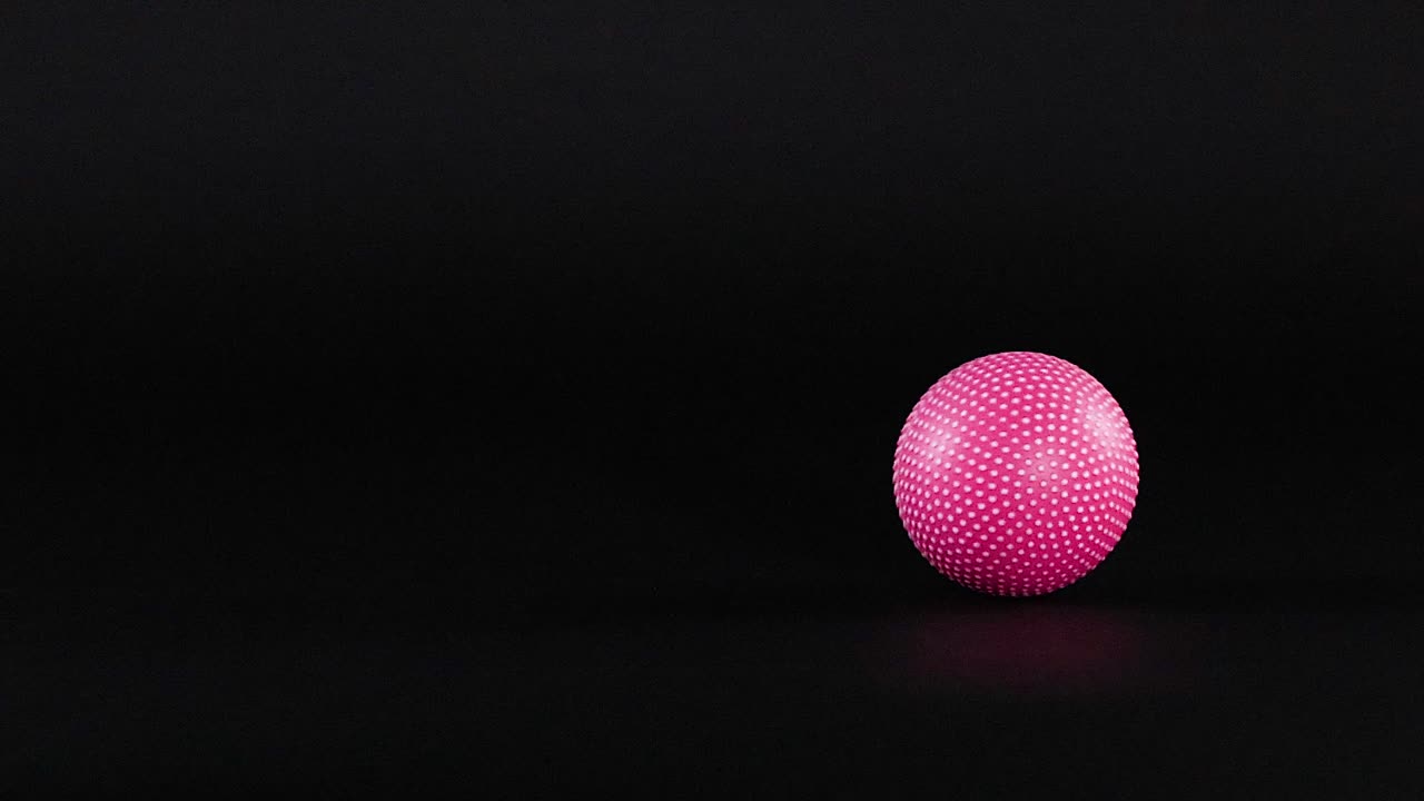 A vibrant pink textured ball rolls smoothly across a dark, minimalist background with soft lighting