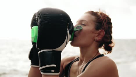 thirsty female boxer in gloves taking a break drinking from the water bottle after training. beautiful woman training by the sea