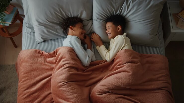 Due bambini che sorridono e legano a letto