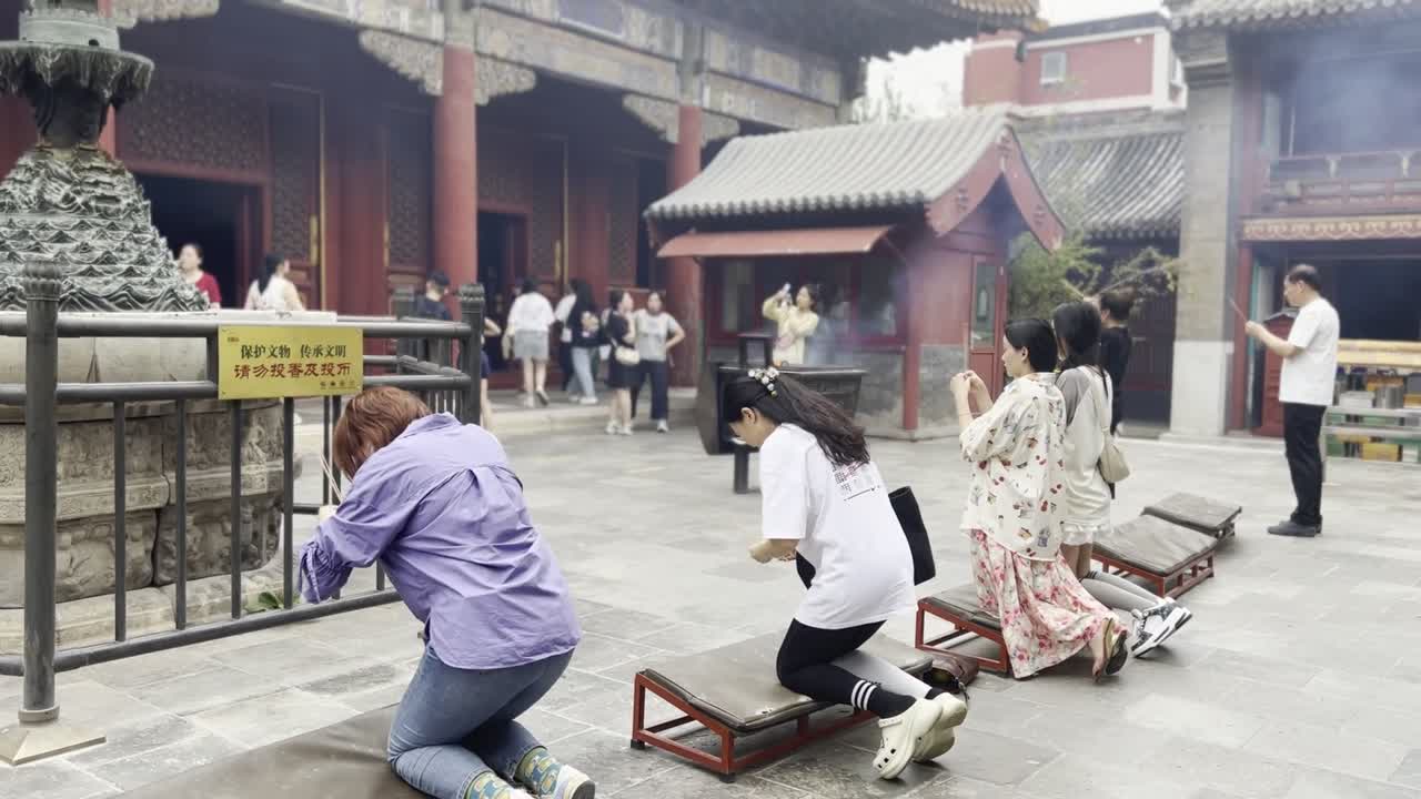 Chinese women praying on their knees with incense inside temple