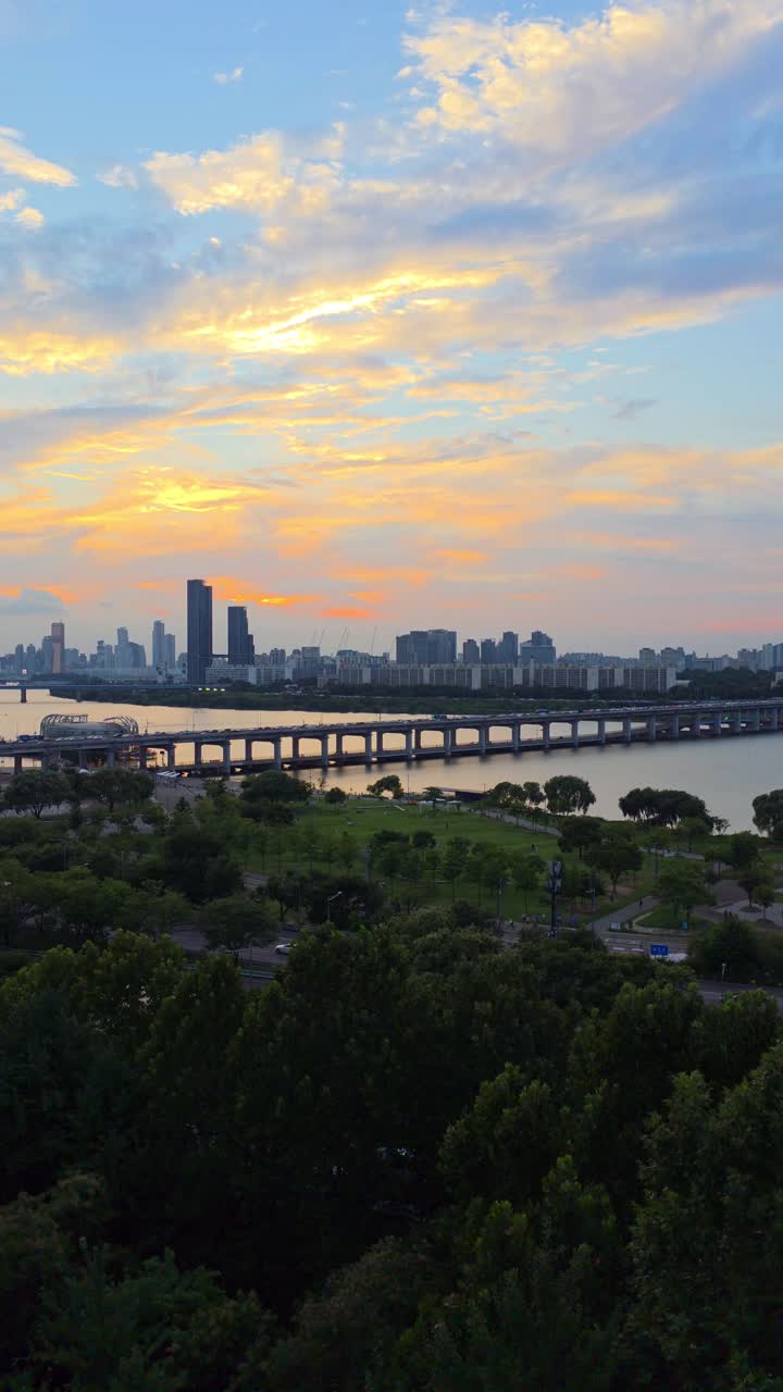 Aerial vertical view of Seoul skyline at sunset with Banpo Bridge traffic crossing the Han River and green park areas in the foreground