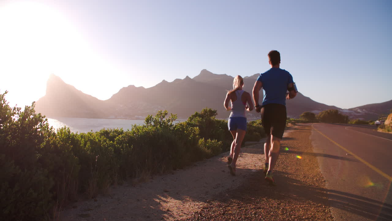 hombre y mujer corriendo por una carretera vacía, cámara lenta, vista trasera