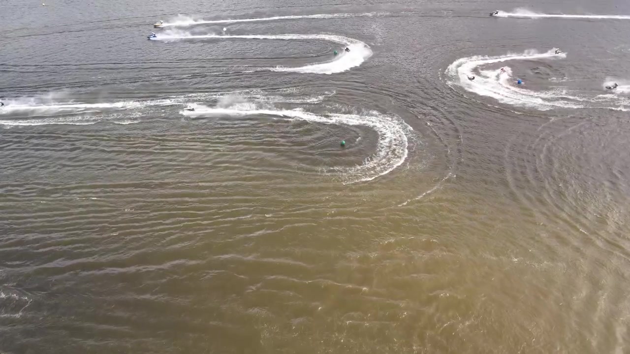 Flere vannscootere kjører raskt over overflaten av en innsjø, og skaper krusninger og bølger i vannet. Scenen fanger spenningen ved vannsport på en rolig innsjø.