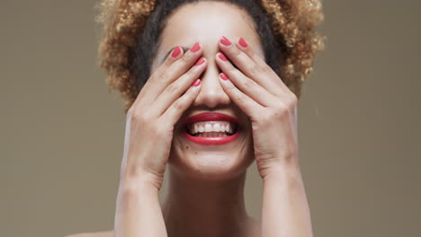 feliz mujer biracial con cabello oscuro y labios y uñas rojas en fondo beige, cámara lenta