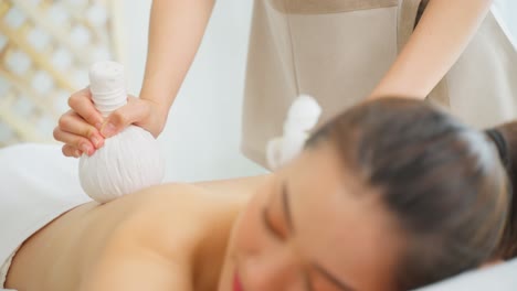 woman receiving herbal ball back massage at spa