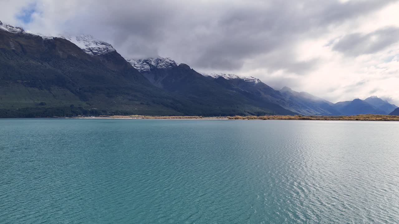 Tranquil lake with mountain backdrop under cloudy skies, showcasing natural beauty and calmness in Glenorchy, New Zealand