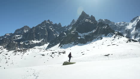 Fotógrafa-Caminando-Sobre-La-Nieve-Y-Pisando-Roca-Bajo-Las-Colinas-Del-Mont-Blanc,-Alpes-Franceses-En-El-Soleado-Día-De-Primavera