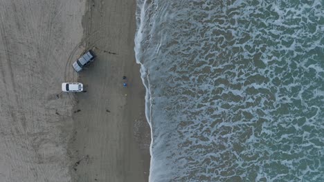 Toma-Aérea-De-Arriba-Hacia-Abajo-De-Un-Pescador-De-Surf-Y-Camiones-En-Pismo-Beach,-California,-Al-Amanecer.