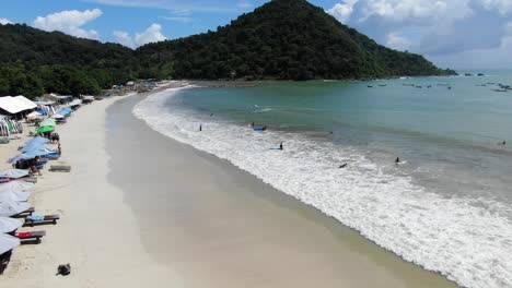 surf paradise with a long sandy beach on a tropical island on a sunny day, waves hitting the shore as surfers heading out to the open ocean