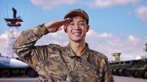 primer plano de un soldado asiático saludando y sonriendo mientras está de pie en un campamento militar