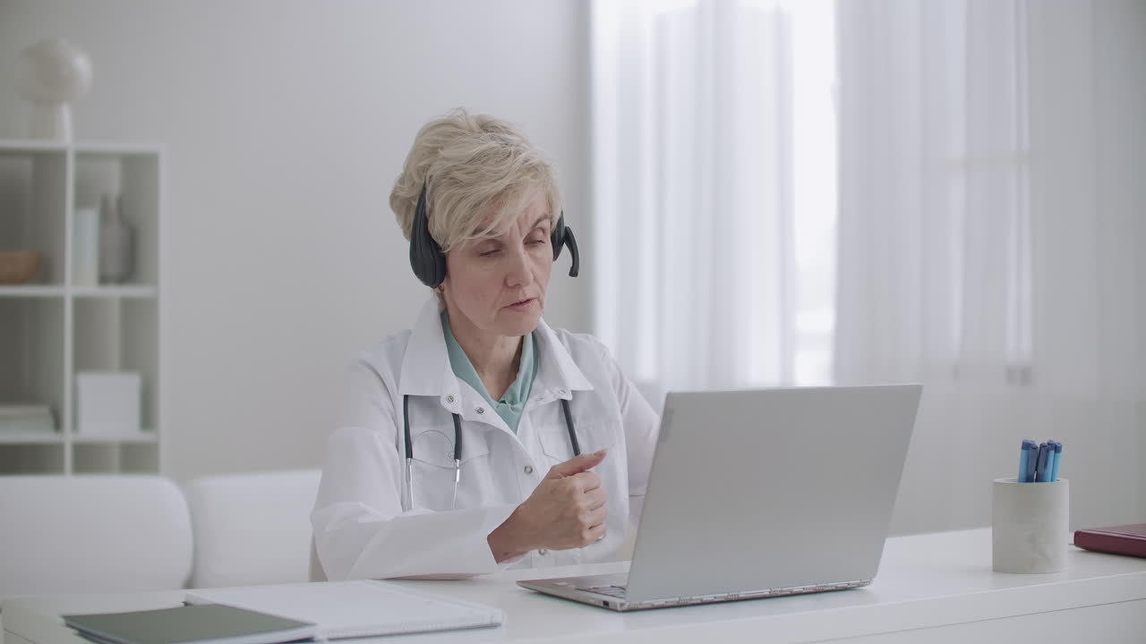 cita en línea con un terapeuta mujer de edad está sentada en la oficina en la clínica y consultando a la gente de forma remota por internet