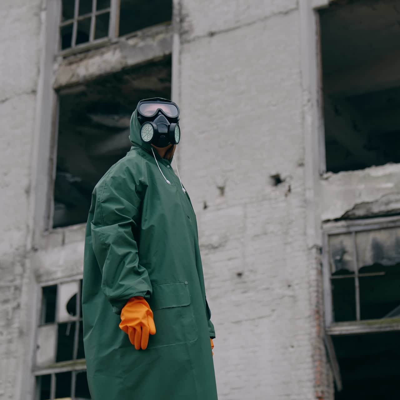 Man in protective clothing and a gas mask is standing on the background of ruined building. The concept of a post-apocalyptic world