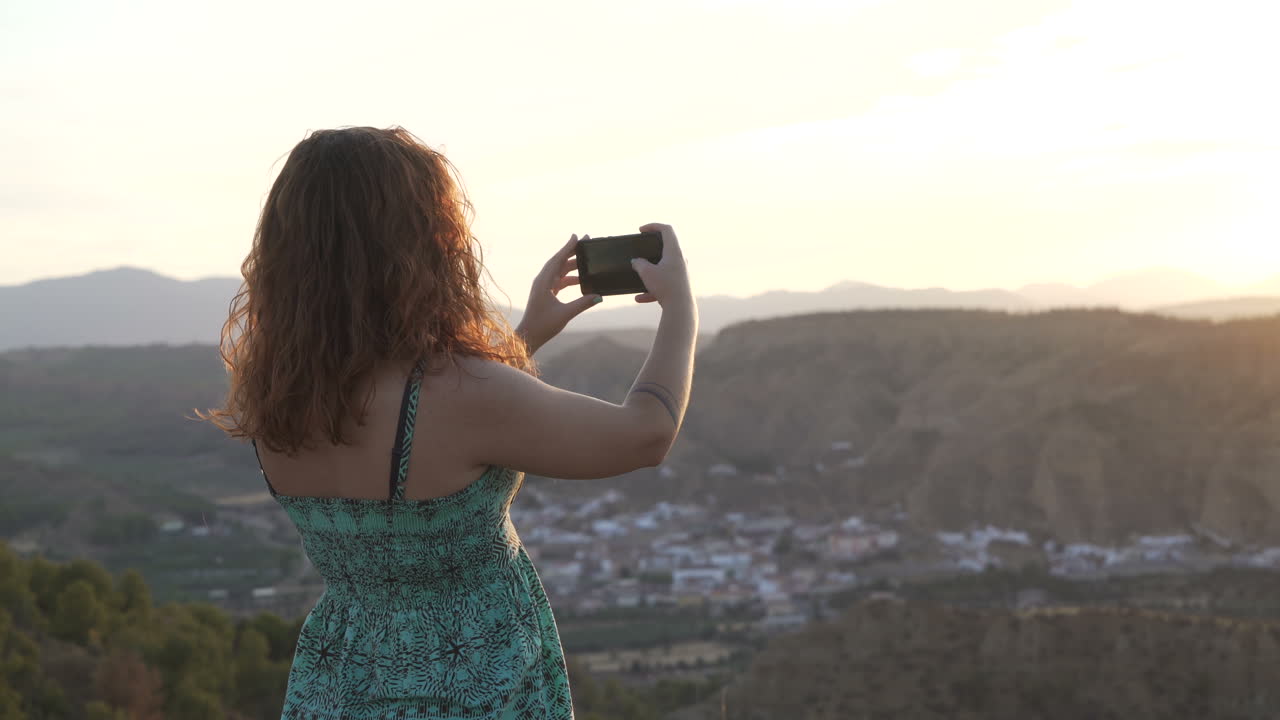 Woman taking photos of a scenic landscape at sunset