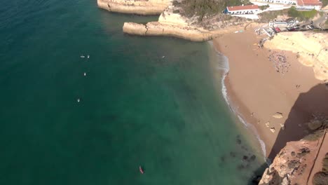 the beautiful waves of benagil, portugal with tourists enjoying the sunlight and boat adventures on the clean, transparent waters of the sea - aerial shot