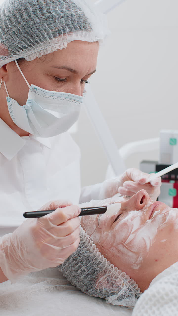 esteticista aplicando una máscara de crema hidratante química médica en el rostro de una mujer joven adulta