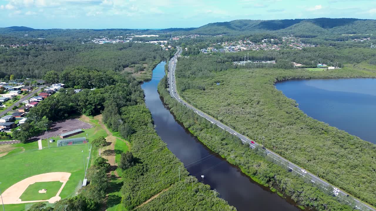Paesaggio aereo ripreso da drone del traffico veicolare che percorre un'autostrada principale, circondato dai corsi d'acqua di Erina Creek e alberi della boscaglia, nei sobborghi della cittadina rurale di East Gosford, Central Coast, Australia.