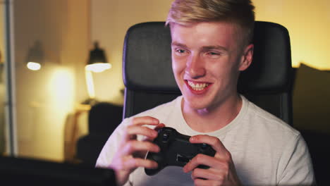 teenage boy sitting in chair in front of screen at home holding computer controller and gaming