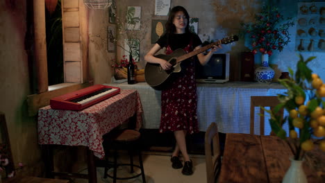 Cute-and-young-Asian-woman-singing-and-playing-guitar-at-home,-Long-shot