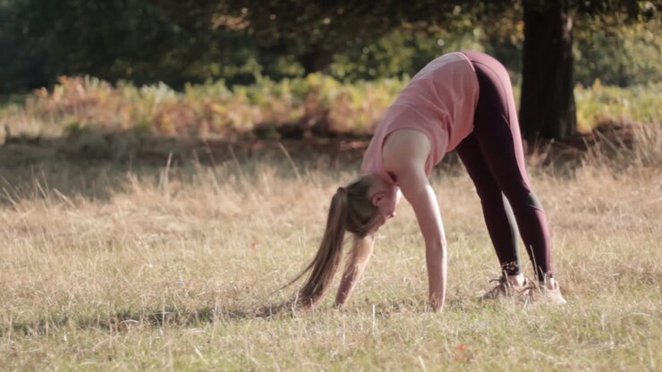 In una giornata di sole, una donna esegue la posizione yoga del cane a testa in giù nel parco all'aperto