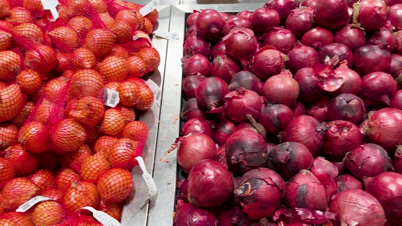 Panning shot of bulk red and yellow onions in a Blue Mountains supermarket produce section.
