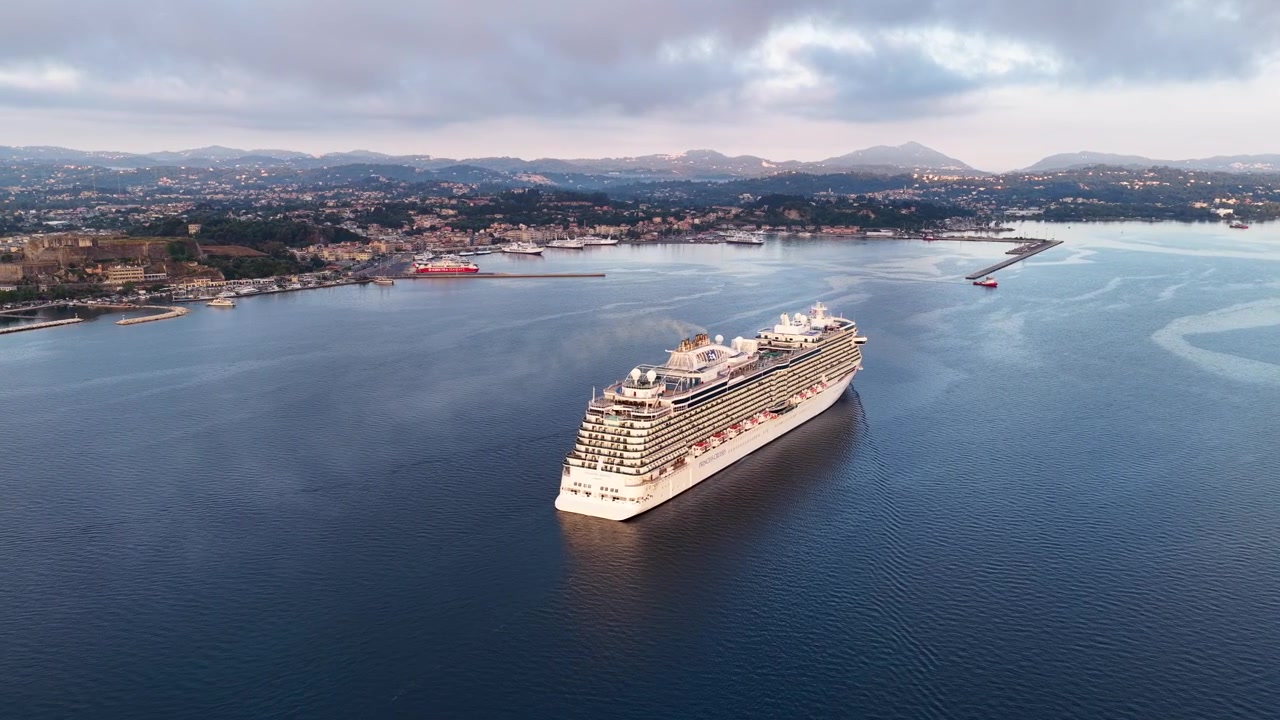 Veduta aerea dall'alto di una grande nave da crociera di lusso che naviga nelle acque calme vicino alla costa storica di Corfù, Grecia, durante una vivace alba mattutina
