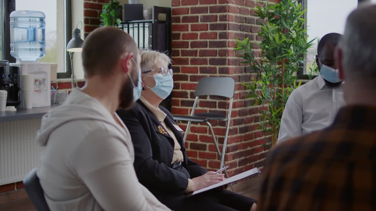 Psychiatrist having conversation with people at aa group meeting for therapy session, wearing face mask